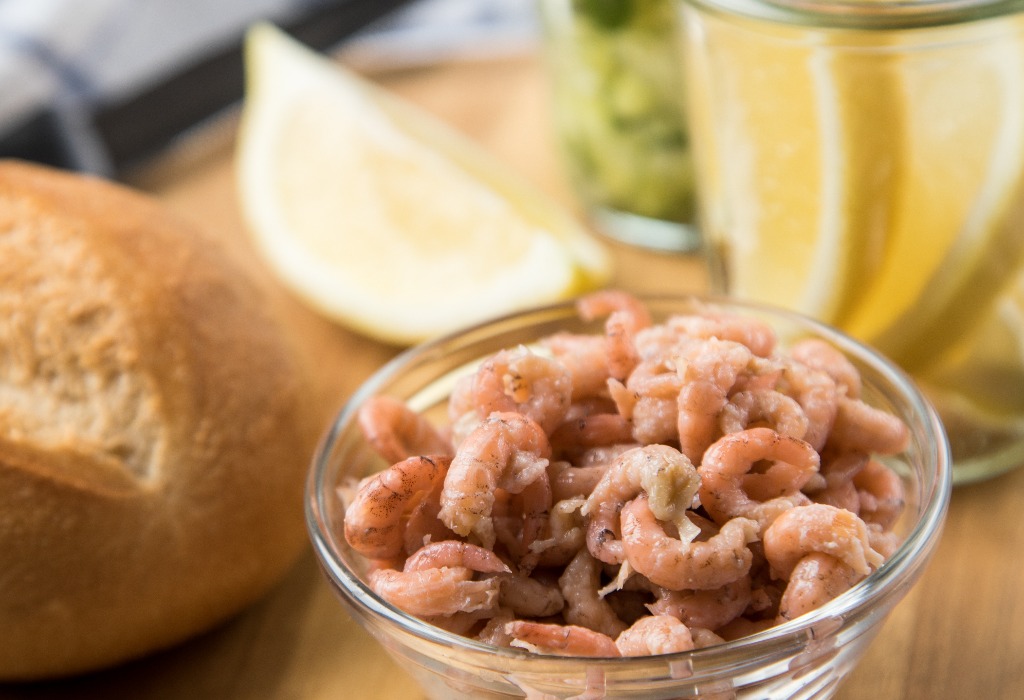 Norddeutsche Friesische Nordseekrabben in Glas Schale mit Brötchen, Gurkensalat und Zitronen auf Holz Brett